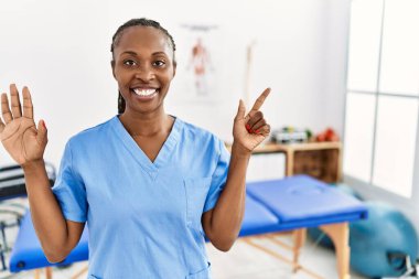 Saçları örgülü zenci bir kadın ağrı kesici kliniğinde çalışıyor. Yedi numaralı parmaklarını gösterip işaret ederken kendine güvenen ve mutlu bir şekilde gülümsüyor.. 