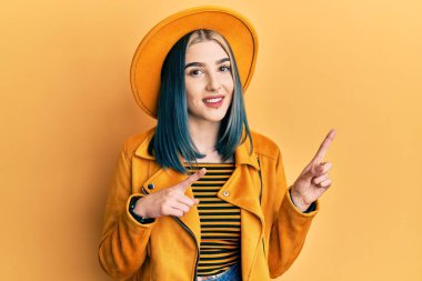 Sarı şapkalı, deri ceketli, gülümseyen ve kameraya bakan genç ve modern bir kız.. 