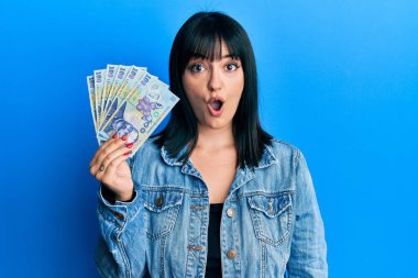 Genç İspanyol kadın elinde 100 Romen parası tutuyor. Korkmuş ve şaşkın bir şekilde ağzı açık kalmış, inançsız bir yüz. 
