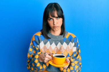 Latin kökenli genç bir kadın bir fincan kahve içiyor şüpheci ve gergin, sorun yüzünden surat asıyor. negatif kişi. 