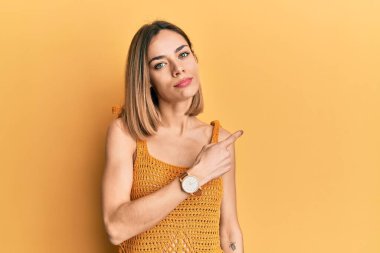 Sıradan sarı tişörtlü, genç, beyaz tenli bir kadın. El parmağı yanda, ciddi ve sakin bir yüz ifadesi var. 