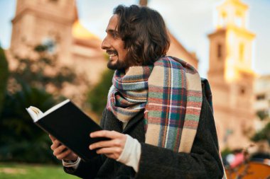 Genç İspanyol adam gülümsüyor, şehirde mutlu bir kitap okuyor..