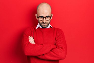 Gündelik kıyafetler giyen, gözlüklü, kuşkucu ve gergin genç kel bir adam. Yüzünde çapraz kollu tasvip etmeyen bir ifade var. negatif kişi. 