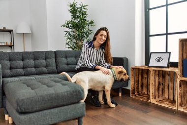 Genç İspanyol kadın evde köpekle kanepede otururken kendinden emin gülümsüyor.