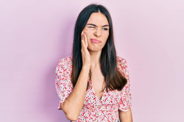 Yazlık elbise giyen esmer bir kadın diş ağrısı ya da diş hastalığından dolayı acı dolu bir ifadeyle dudaklarına dokunuyor. dişçi 