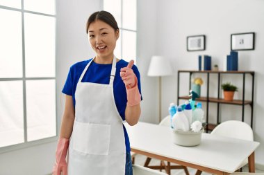 Temiz üniforma giyen genç Çinli kız mutlu ve pozitif gülümsüyor, başparmağıyla mükemmel ve onay işareti yapıyor. 