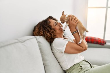 Orta yaşlı İspanyol kadın gülümsüyor, elinde Chihuahua ile.