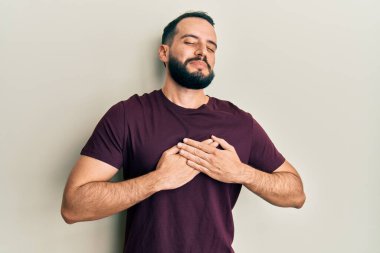 Sakallı, sıradan tişörtler giyen, elleri göğsünde, gözleri kapalı, yüzünde minnet ifadesi olan genç bir adam. sağlık kavramı. 