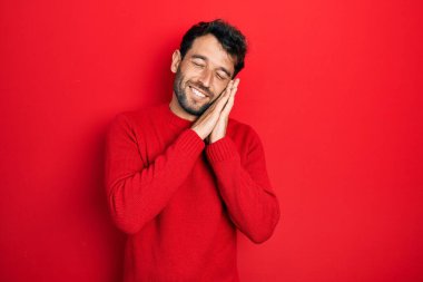 Sakallı, sıradan kırmızı bir kazak giyen, yorgun uyuyan, hayal kuran ve elleriyle poz veren, gözleri kapalı yakışıklı bir adam.. 