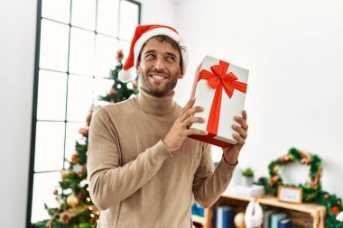 Evde kendine güvenen genç İspanyol adam Noel hediyesini tutuyor.