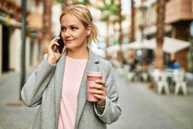 Sarışın iş kadını akıllı telefondan konuşuyor. Şehirde kahve içiyor..