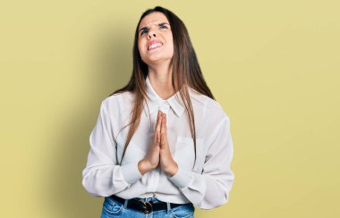 Genç esmer kız beyaz iş gömleği giyiyor. Elleriyle yalvarıyor ve dua ediyor. Yüzünde umut ifadesi var. Yalvarıyor. 