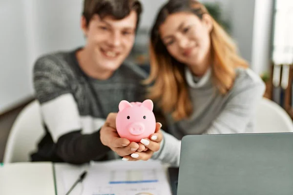 Jovem Casal Caucasiano Sorrindo Feliz Segurando Porquinho Banco Sentado Mesa — Fotografia de Stock