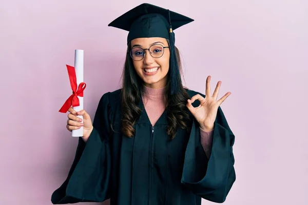 Young Hispanic Woman Wearing Graduation Uniform Holding Diploma Doing Sign — 스톡 사진