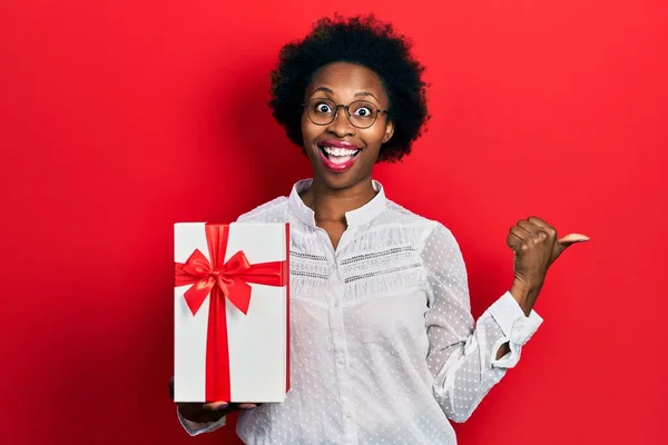 Joven Mujer Afroamericana Sosteniendo Regalo Señalando Pulgar Hacia Lado Sonriendo — Foto de Stock