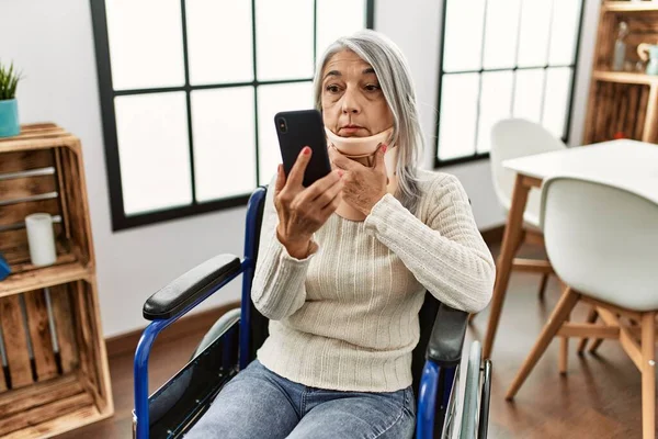 Orta yaşlı, kır saçlı, evinde tekerlekli sandalyede oturan bir kadın.