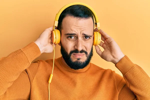 問題のために動揺を眉をひそめ ヘッドフォン懐疑的かつ神経を使用して音楽を聞いてひげを持つ若い男 否定的な人 — ストック写真