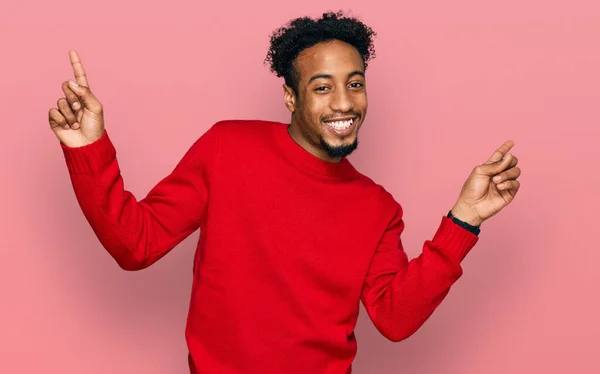 カジュアルな冬のセーターを着てひげを生やした若いアフリカ系アメリカ人男性は さまざまな方向に指で自信を持って指して笑顔 広告のコピースペース — ストック写真