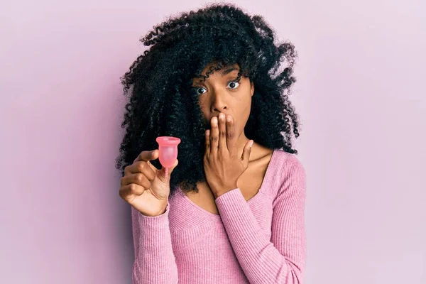 Afroamerykanka Afro Włosami Trzymająca Kubek Miesiączkowy Zakrywający Usta Ręką Zszokowana — Zdjęcie stockowe