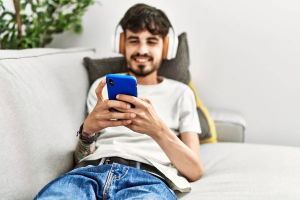 Молодий Іспаномовний Чоловік Використовує Смартфон Навушники Лежать Дивані Вдома — стокове фото