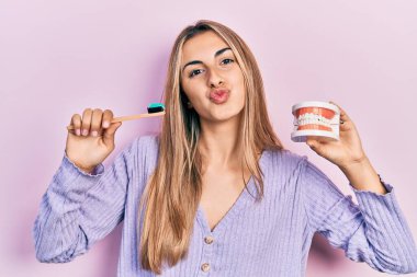 Güzel İspanyol bir kadın takma diş ve diş fırçasıyla kameraya bakıp öpüşürken sevimli ve seksi görünüyor. aşk ifadesi. 