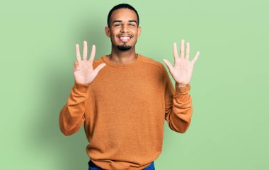 Genç, Afro-Amerikalı, günlük kıyafetler giymiş, dokuz numaralı parmaklarıyla işaret ederken, kendinden emin ve mutlu bir şekilde gülümsüyor.. 