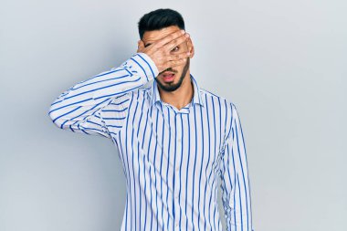 Sakallı, sıradan çizgili tişörtlü genç İspanyol bir adam. Şok olmuş, yüzünü ve gözlerini kapamış, utangaç ifadesiyle parmaklarının arasından bakıyor.. 