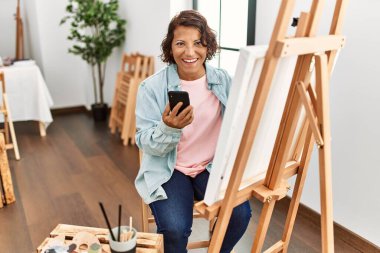 Sanat stüdyosunda akıllı telefon çizimi yapan orta yaşlı İspanyol bir kadın..