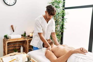 İki İspanyol erkek terapist ve hasta güzellik merkezinde yüz masajı yapıyorlar.