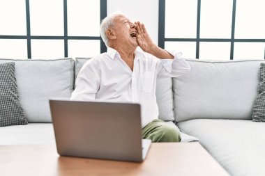 Evde dizüstü bilgisayar kullanan kıdemli bir adam kanepede oturup el pençe divan bağırıyor ve el pençe divan bağırıyordu. iletişim konsepti. 