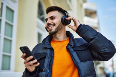 Yakışıklı, sakallı, neşeli, kendine güvenen, kışlık palto giyen, akıllı telefondan müzik dinleyen bir İspanyol.