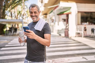 Orta yaşlı İspanyol adam spor giyer. Sokakta akıllı telefon kullanır.