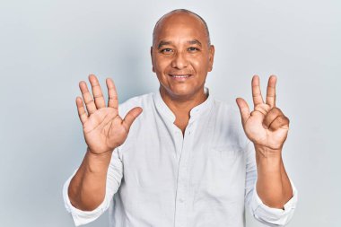 Orta yaşlı, gündelik kıyafetler giyen Latin bir adam 8 numaralı parmaklarını gösterip işaret ederken kendinden emin ve mutlu bir şekilde gülümsüyor.. 