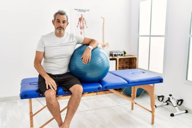 Orta yaşlı İspanyol bir adam ağrı kesici kliniğinde elinde pilates topu tutarken yüzünde ciddi bir ifadeyle rahatlıyor. Basit ve doğal bir şekilde kameraya bakıyorsun.. 