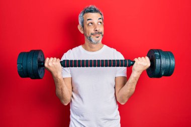 Yakışıklı, orta yaşlı, gri saçlı spor giysili, halterli, gülümseyen bir adam.. 