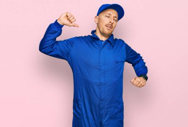 Kel, sakallı, işçi tulumu giyen, yorgun, rahat, uykulu ve sabahın erken saatlerinde esneyen bir adam. 