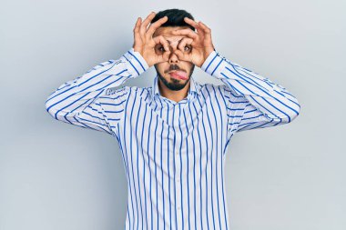 Sakallı, sıradan çizgili tişörtlü genç bir İspanyol dürbün gibi jest yapıyor, gözleri parmaklarından bakıyor. çılgın ifade. 