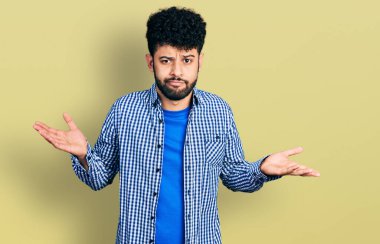 Sakallı, sıradan tişörtlü, kafası karışık, kolları açık, hiçbir fikri olmayan, şüpheli yüzlü genç bir Arap.. 