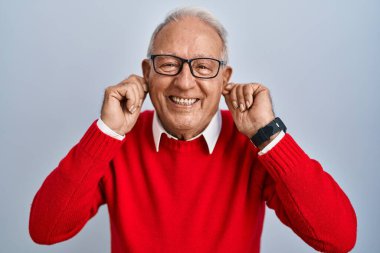 İzole edilmiş arka planda gri saçlı yaşlı adam gülümseyerek parmaklarıyla kulaklarını çekiyor, komik bir jest. deneme sorunu 