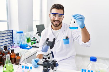 Laboratuvarda deney tüpü tutan bilim adamı üniforması giyen İspanyol genç adam.