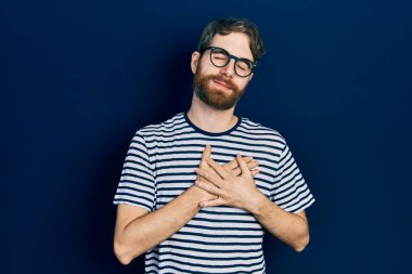 Sakallı, çizgili tişörtlü, gözlüklü, göğsünde elleri kapalı, yüzünde minnet ifadesi olan beyaz bir adam. sağlık kavramı. 