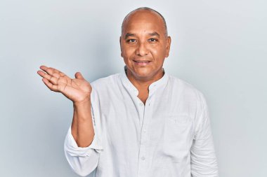 Orta yaşlı, sıradan kıyafetler giyen, neşeli gülümseyen, el ele tutuşup kameraya bakan Latin bir adam.. 