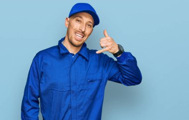 Sakallı, inşaatçı tulumu giymiş, kel bir adam. Gülümsüyor, telefonla el ve parmak hareketleri yapıyor. Telefonda konuşuyor gibi. iletişim kavramları. 