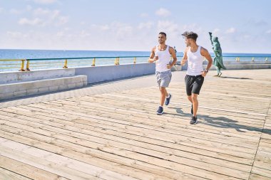 İki İspanyol erkek, sportif, gülümseyen bir çift, deniz kenarında koşuyorlar.