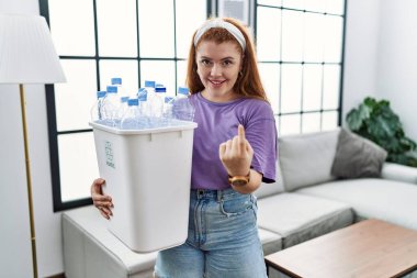 Genç kızıl saçlı kadın elinde plastik şişelerle çöpleri geri dönüşüm sepetine koyuyor. El hareketleriyle bizi mutlu etmeye ve gülümsemeye davet ediyor. 
