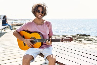Genç İspanyol adam klasik gitar çalıyor sahilde bankta oturuyor..