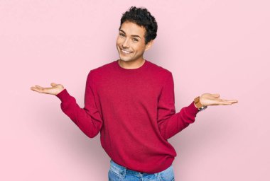 Gündelik kıyafetler giyen, gülümseyen, iki elini de açık tutan, sunan ve reklam karşılaştırması yapan genç yakışıklı bir adam. 