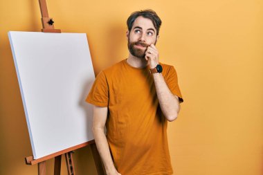 Kafkasyalı sakallı bir adam boyacı sehpasının yanında durup parmak çenesinde şüpheyi düşünüp kafasını kaldırıyor. 