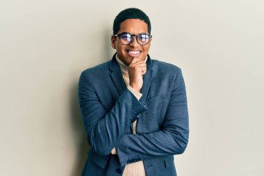 Zarif kıyafetler giyen ve gözlüklü yakışıklı genç adam kameraya kendinden emin bakıyor kollarını kavuşturmuş ve çenesini kaldırmış şekilde gülümsüyor. Olumlu düşünmek. 