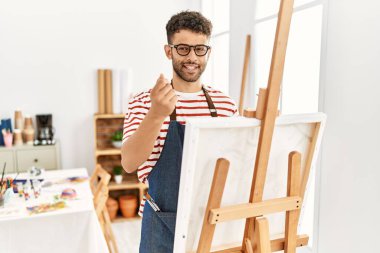Arab young man at art studio doing money gesture with hands, asking for salary payment, millionaire business 